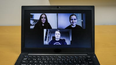 En laptopdator på ett bord. På skärmen syns tre unga personer i ett videosamtal.