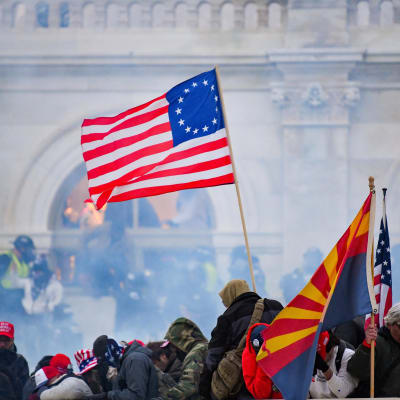 USA:s flagga vajar över en folkmassa framför kongressbyggnaden i Washington. Luften är dimmig av tårgas.