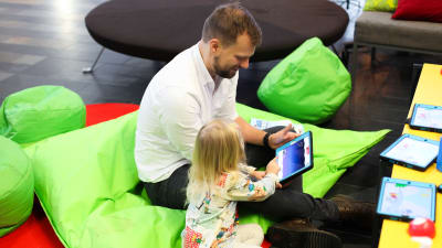 En förälder och ett barn spelar på en iPad