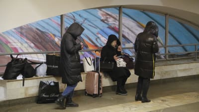Tre svartklädda människor väntar på metron i Kiev, Ukraina. De har flera väskor med sig.