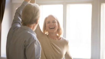En äldre man och kvinna dansar leende hemma.