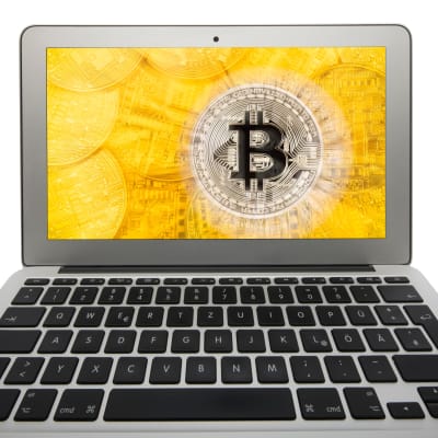 Foto av laptop, på skärmen en bild som föreställer guldfärgade mynt samt ett silverfärgat mynt med symbolen för Bitcoin.