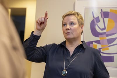 Anu Sajavaara, en kvinna, står med ena fingret upp mot taket.