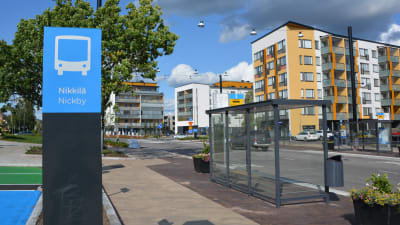 Till vänster syns en skylt som det står Nickby på, till höger syns en busshållplats invid Stora Byvägen. Det är en del av Nickby bussterminal som syns.