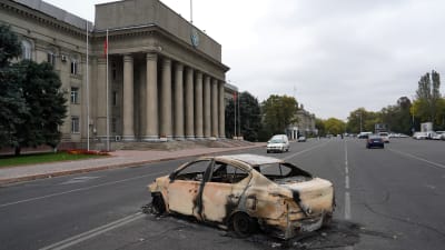 En utbränd bil på gatan framför en palatsliknande byggnad