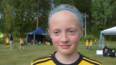 Ella Ginström, en flicka med blått hårband och gul fotbollsskjorta.