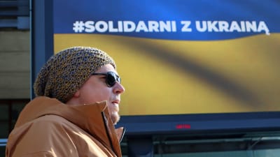 En man står framför en skylt i blågult som uppmanar till solidaritet med Ukraina.