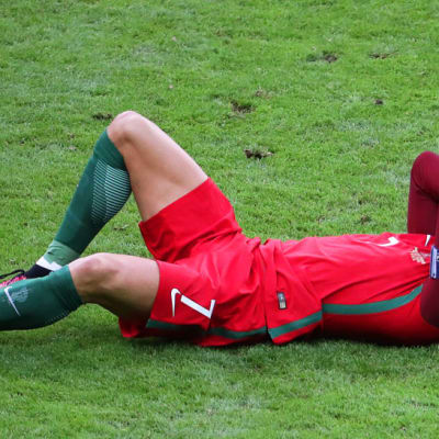 Portugalin Cristiano Ronaldo pitelee kasvojaan nurmen pinnassa.