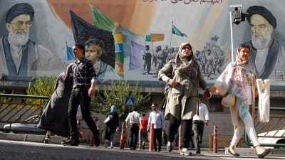 Iranier passerar en väggmålning med iranska martyrer och andliga ledare. Bilden tagen den 22 juli 2018 i Teheran. 
