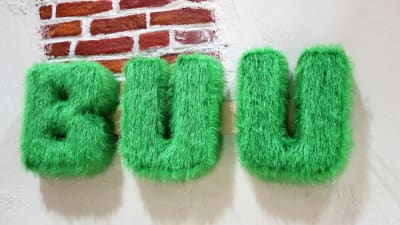 barnprogrammet BUU-klubbens logo. Tre gröna och fluffiga bokstäver B U och U mot en rappad tegelvägg
