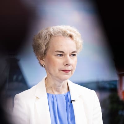 En kvinna klädd i blått och vitt med kort lockigt hår tittar snett neråt.