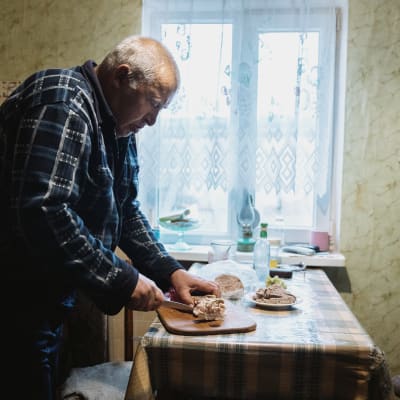 Mies leikkaa lihaa ruokapöydän ääressä.