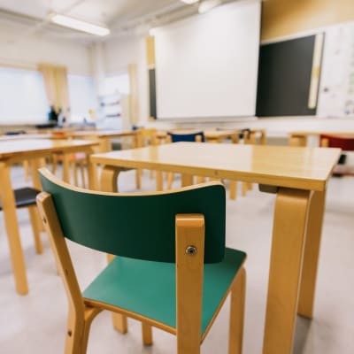 Ett tomt klassrum där stolar, pulpeter och en svart tavla syns.