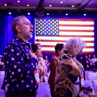 Flera personer står med högra handen på bröstet. Bakom dem syns en amerikansk flagga. 