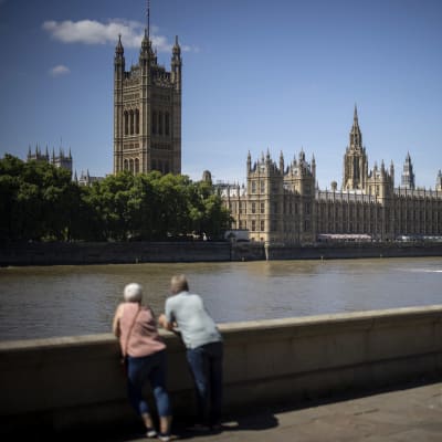 Pariskunta katsoo Lontoon halki virtaavaa Thames-jokea, jonka takana näky Westminsterin palatsi.