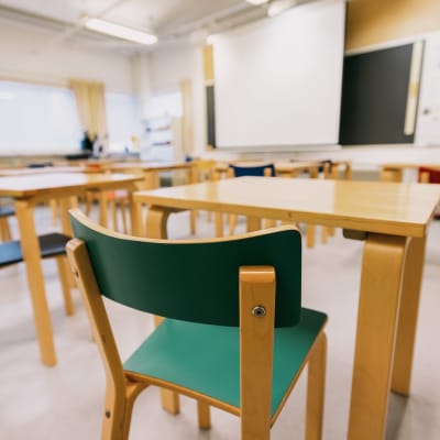 Ett tomt klassrum där stolar, pulpeter och en svart tavla syns.
