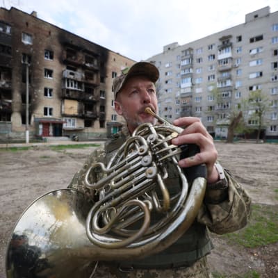 Ukrainalainen sotilas soittaa tuhoutuneen rakennuksen edessä käyrätorvea