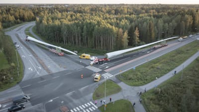 Flygfoto av två rotorblad som transporteras med lastbilar längsmed en landsväg i Karleby.