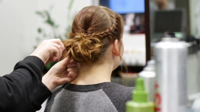 En frisör lagar en uppsättning med flätor åt en ung kvinna.
