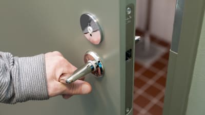 Käsi tarttuu vessan oven kahvaan.