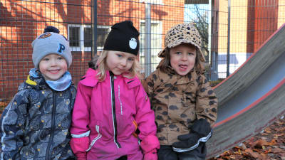 Tre varmt klädda dagisbarn vid rutschkana.