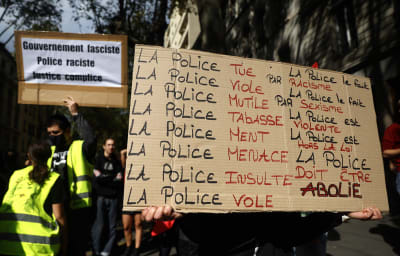Närbild av en skylt med text på där det står att polisen är våldsam. I bakgrunden syns också en annan skylt.