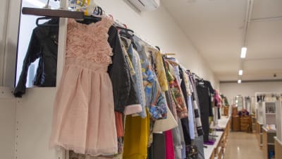 En rosa barnklänning hänger på en stång tillsammans med en massa andra kläder. Kläderna är till salu i en loppis.