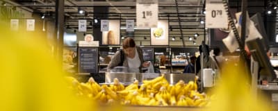 En dam står och väljer bananer i en matbutik.