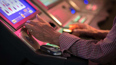 Lähikuva vanhan miehen käsistä pelaamassa rahapelejä Casino Helsingissä.