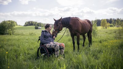 Nicole Hellberg sitter i sin rullstol ute i hagen med sin häst.