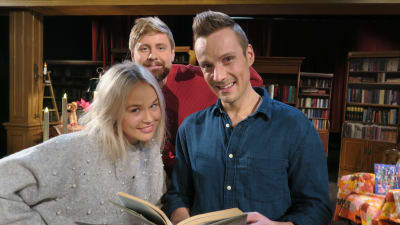 Tre personer poserar framför kameran med en bok.