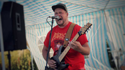 En man i röd skjorta spelar gitarr och skriker i en mikrofon