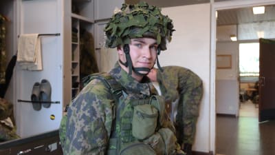 Undersergeant Tuomas Toukosalo i militärstugan iklädd stridsmundering med kamoflagehjälm