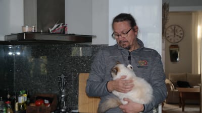 Thomas Lagerroos står i sitt kök med en lurvig katt i famnen