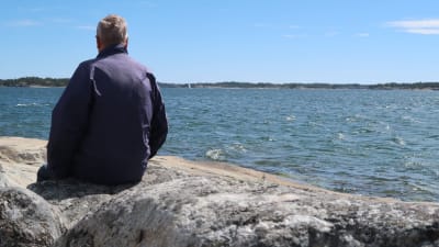 Mies istuu kalliolla katsetta mereen päin