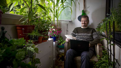 Veli Pekka Toropainen sitter ute på balkongen med sin laptop. Omkring sig har han massor med gröna växter och blommor.