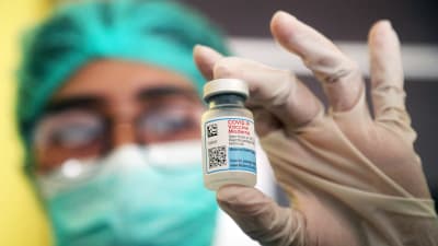 En vårdare håller en vaccinförpackning av Moderna i sin handskbeklädda hand.