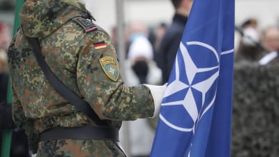 En soldat med Tysklands flagga och ett Nato-märke på armen håller i Natos flagga. 
