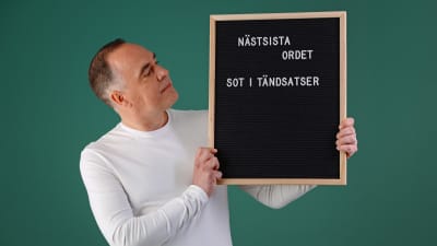 Jens Berg håller i en svart skylt med texten: "Näst sista ordet, sot i tändsatser".