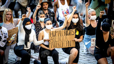 En grupp unga kvinnor knäböjer med en höjd knytnäve. I famnen har de ett plakat med texten Human rights are npt a matter of opinion.