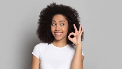 En kvinna ler stort och kniper samman tummen och pekfingret i en gest som betyder ok.