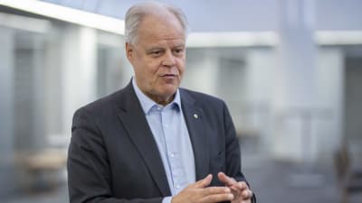 En man i kostym och grått hår pratar och gestikulerar.