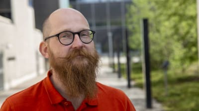Jussi Eronen är en man med långt skägg och runda glasögon. 