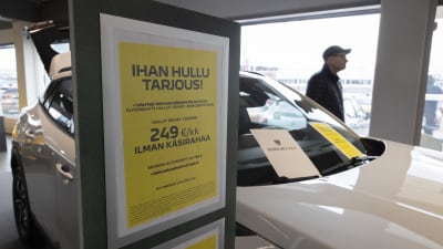 Keltainen tarjouskyltti mainostaa autoleasing tarjousta valkoisen auton kyljessä.