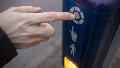 En hand trycker på knappen för trafikljuset vid ett övergångsställe. 