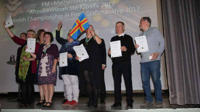 Flera personer står på en scen efter att de fått medaljer i mattävlingen Mathantverk.
