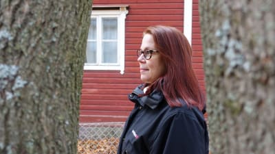 Rödhårig kvinna i profil mot röd husvägg