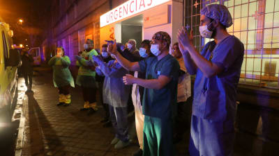 Madridilaisen sairaalan henkilökunta tervehtii suosiotaan osoittavia kansalaisia. Espanjalaisille on viime aikoina tullut tavaksi osoittaa iltaisin parvekkeilla suosiotaan koronavirusta vastaan taisteleville sairaaloiden työntekijöille.