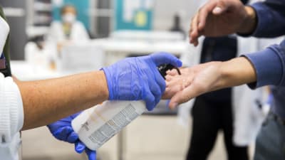 Närbild av händer då en person får desinfektionsmedel för händerna av en person i skyddshanskar. Personer ges desinfektionsmedel för händerna då de kommer in på ett sjukhus.