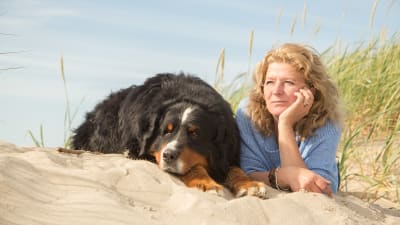Medelålders kvinna ligger i sanden bredvid stor svart hund
